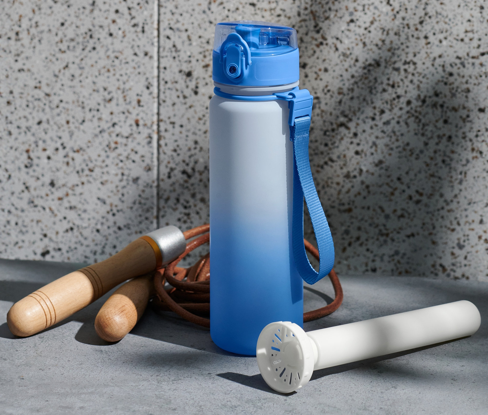 Mavi beyaz bir matara, atlama ipi ve beyaz bir soğutma silindirinin yanında duruyor.