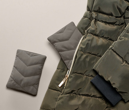 Zeytin yeşili kapitone bir ceketin yanında iki adet cep ısıtma yastığı.