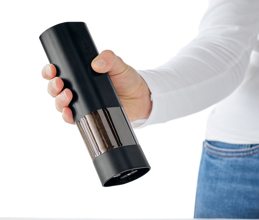 Bir el, beyaz bir masanın üzerinde baharat serpen siyah bir baharat değirmeni tutuyor.