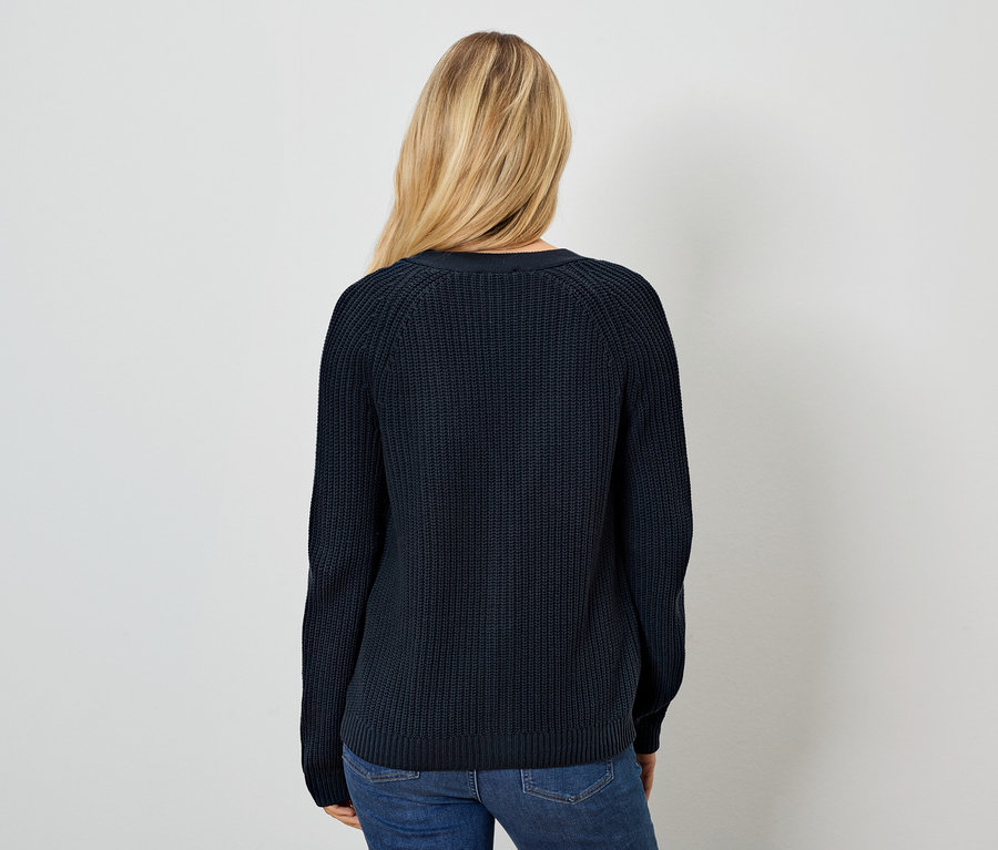 Sırtı kameraya dönük bir kadın, lacivert bir kazak ve kot pantolon giyiyor.