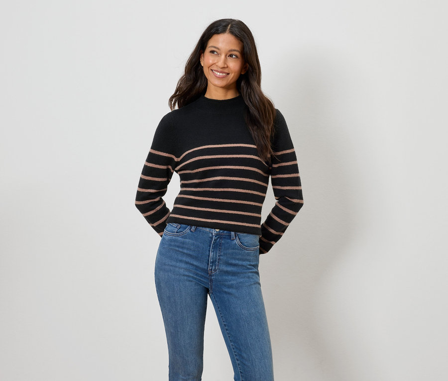 Kadın siyah ve kahverengi çizgili bir kazak ve mavi kot pantolon giyiyor.