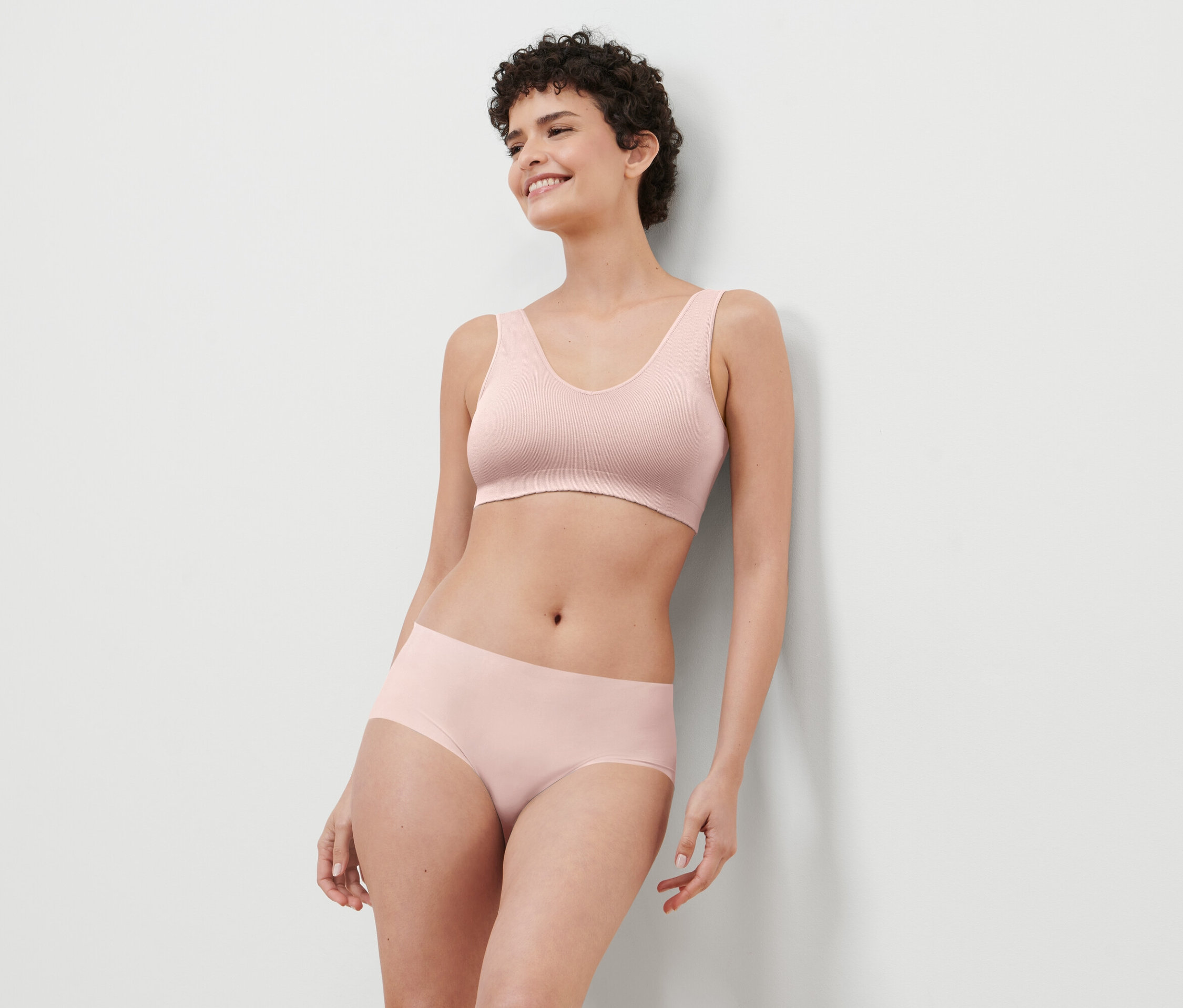 Kısa saçlı bir kadın pembe bir sutyen ve külot giyiyor.