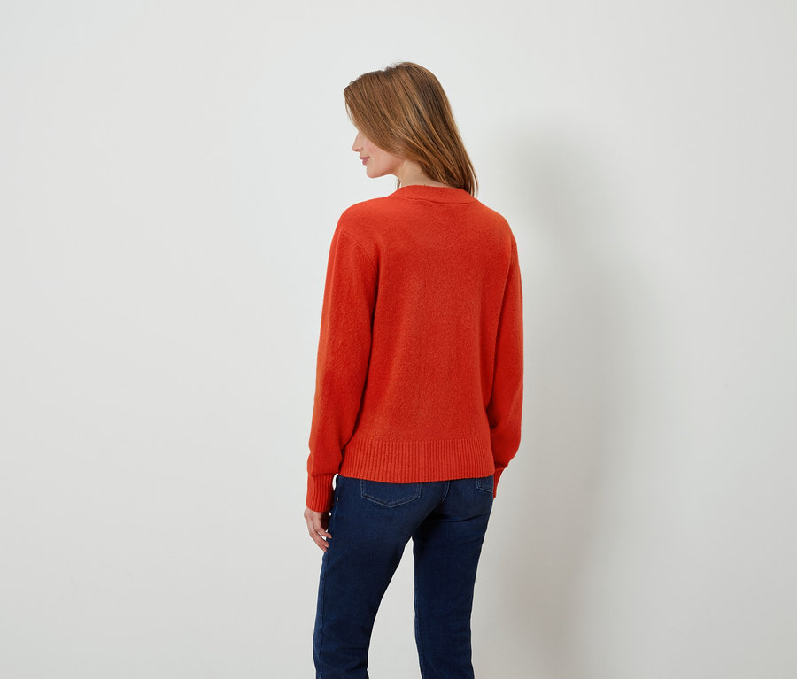 Turuncu kazak ve koyu mavi kot pantolon giyen bir kadın, kameraya arkası dönük duruyor.