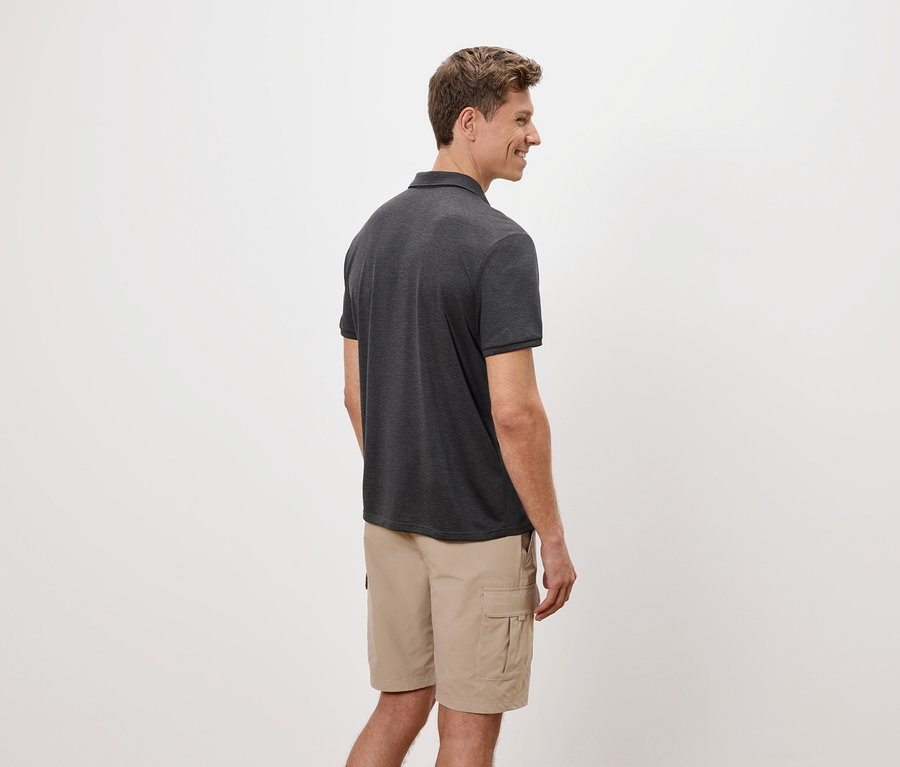 Bir adam yan duruyor, beyaz bir arka plan önünde gri bir polo yaka tişört ve bej rengi kargo şort giyiyor.