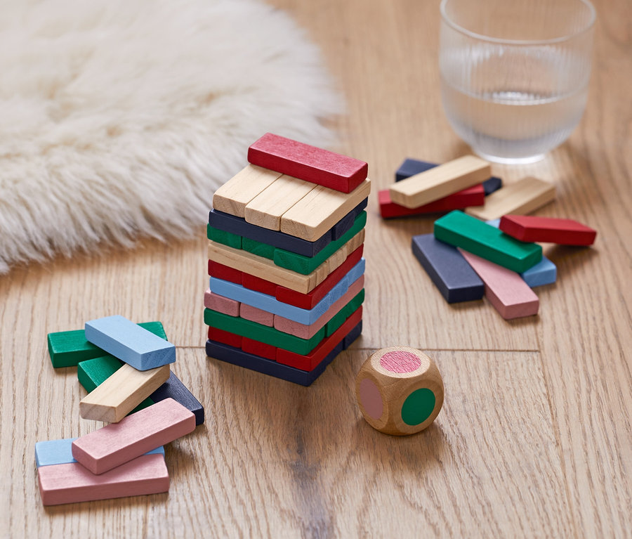 Ahşap zeminde renkli ahşap bloklardan yapılmış bir Mini Ahşap Kule, yanında bir zar ve bir bardak su duruyor.