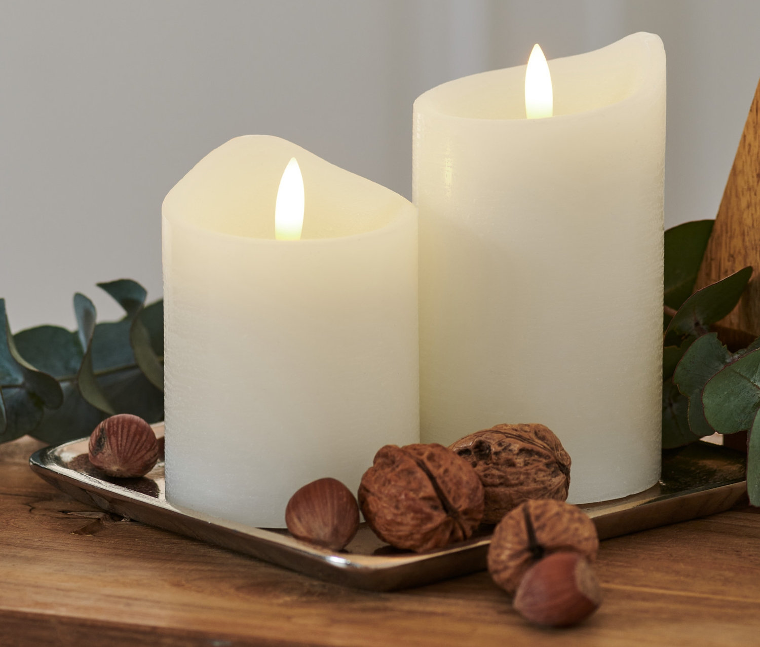 Ahşap bir masanın üzerinde, gümüş bir tepside iki adet beyaz LED mum, fındık ve bir okaliptüs dalı bulunmaktadır.