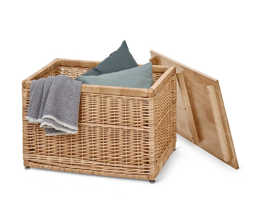 Mavi yastıklar, gri bir battaniye ve açık ahşap kapaklı hasır sandık.