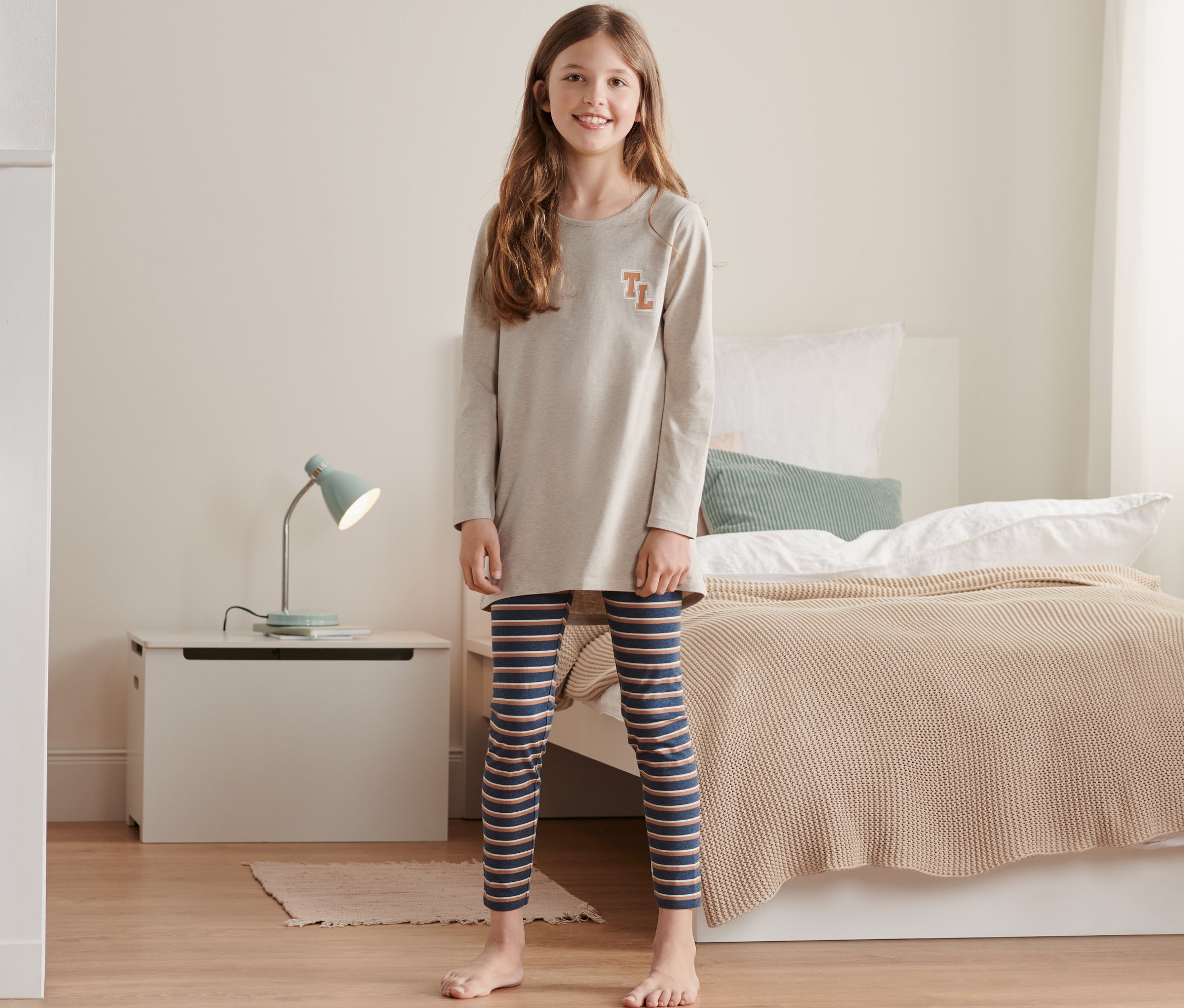 Çizgili taytlı çocuk pijaması içinde duran kız.