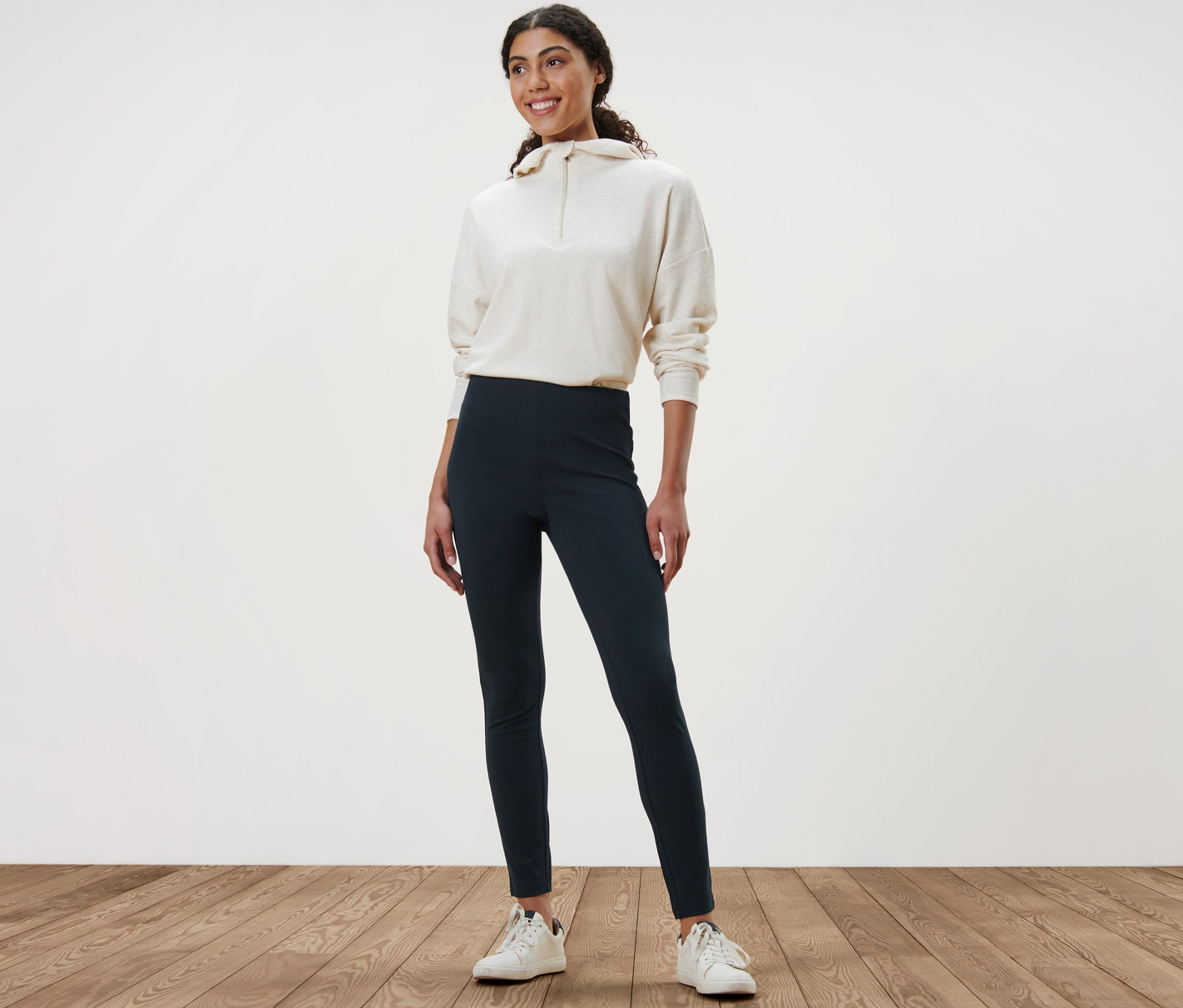 Ahşap zeminde duran bir kadın Kalın Tayt ve sweatshirt giyiyor.