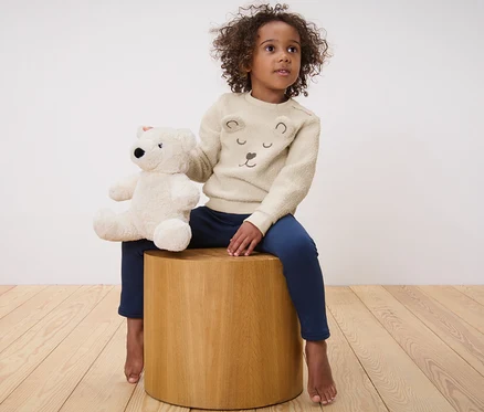 Kız tahta bir taburede oturmuş oyuncak ayı tutuyor. Üzerinde Çocuk Teddy Sweatshirt var.