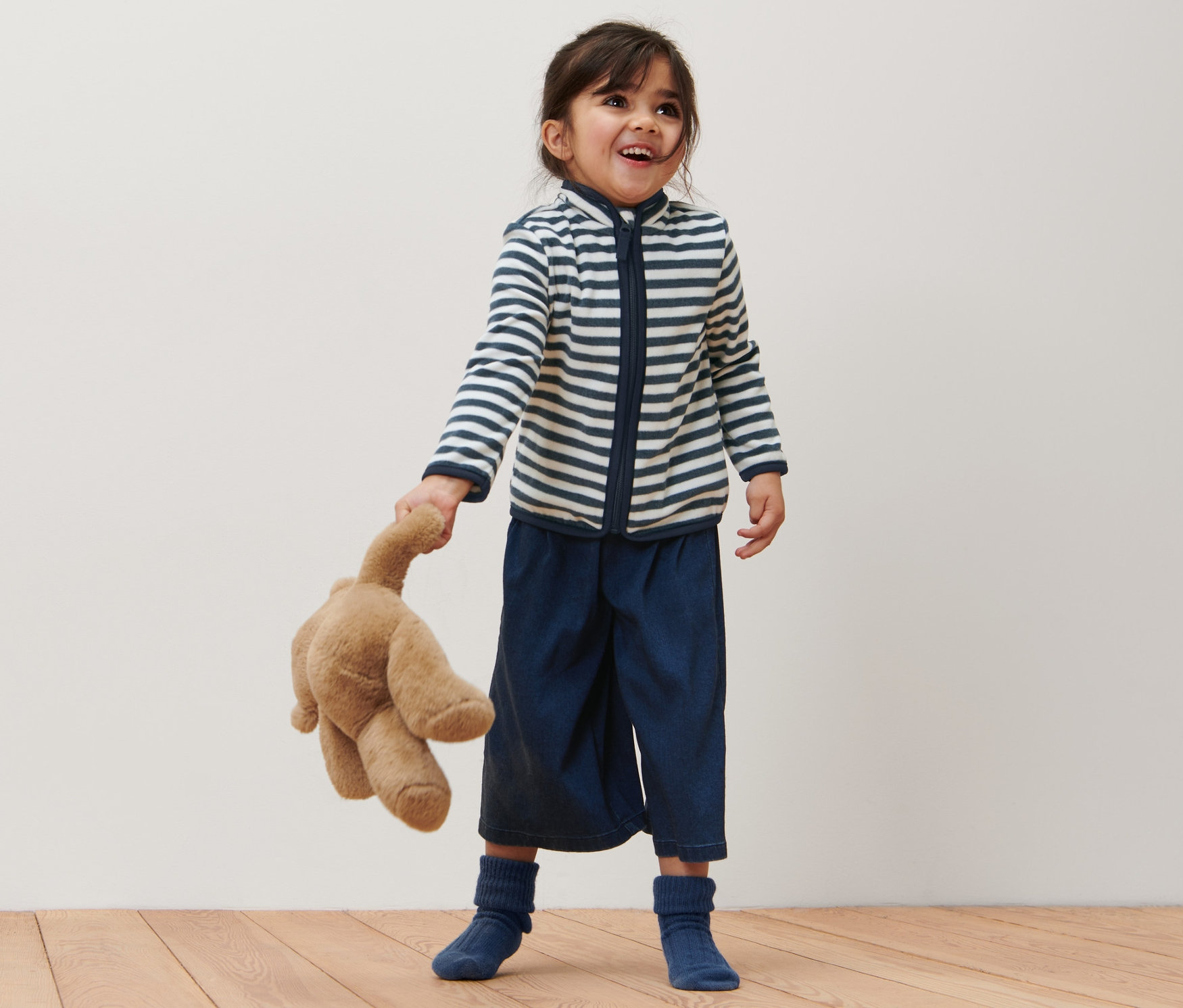 Gülümseyen kız çocuğu oyuncak ayı tutuyor ve Kıvırcık çocuk polar ceket giyiyor.