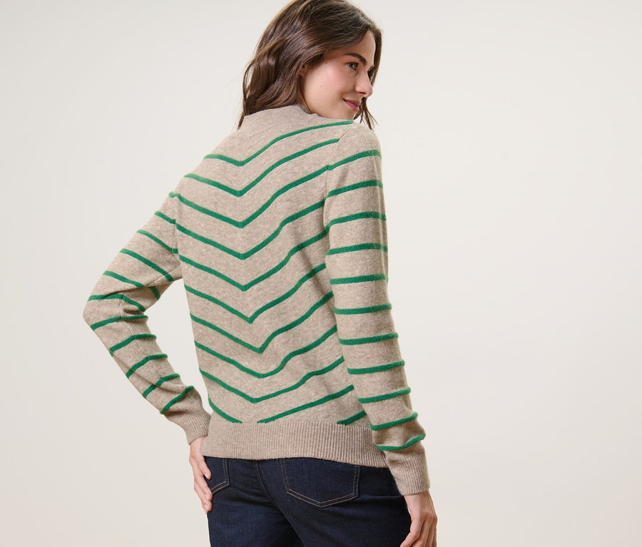 Kadın omzunun üzerinden bakıyor ve krem rengi, dik yakalı, çizgili örgü kazakla poz veriyor.