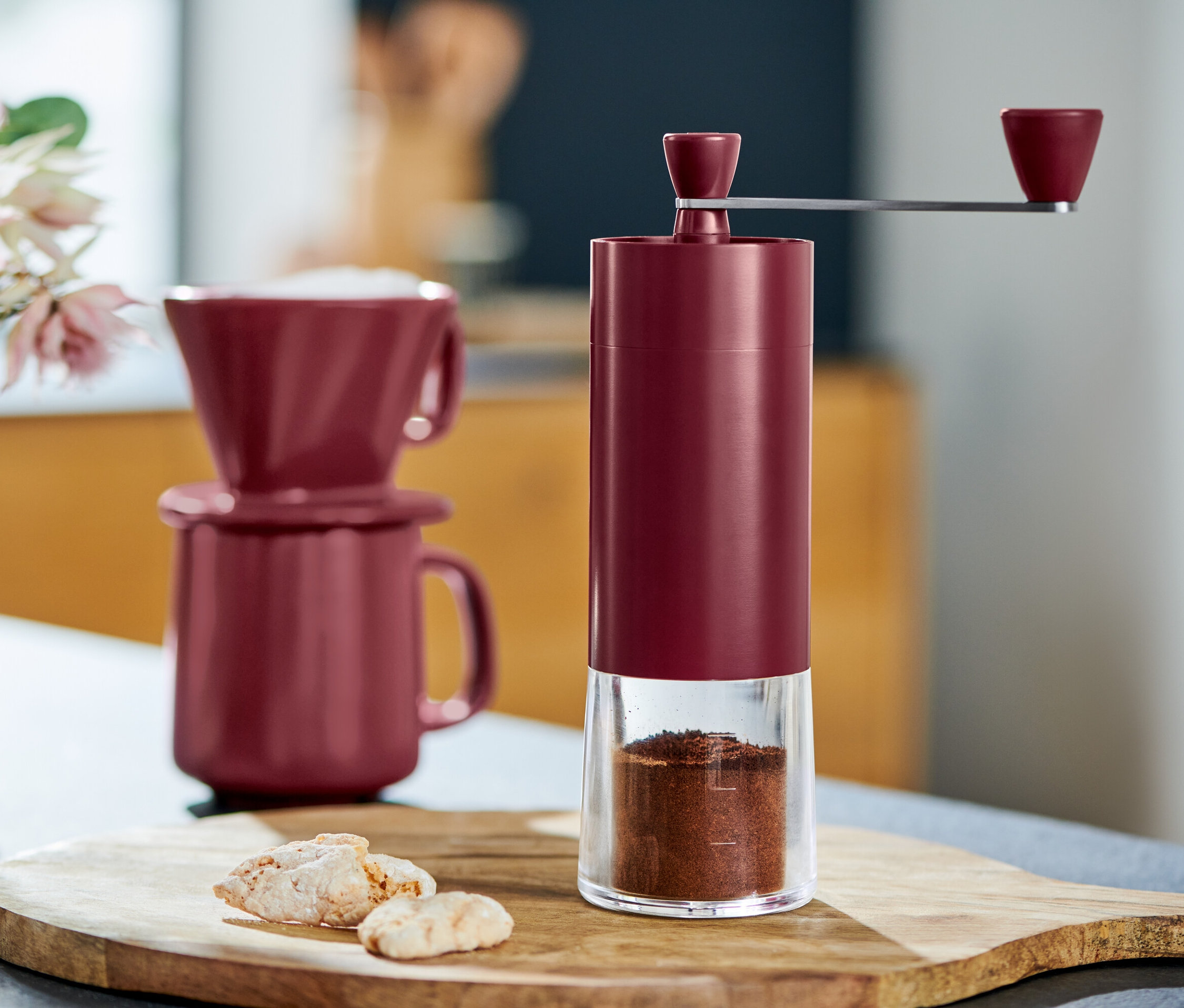 Fincanların ve kurabiyelerin yanında, berry renginde manuel kahve değirmeni detayı.