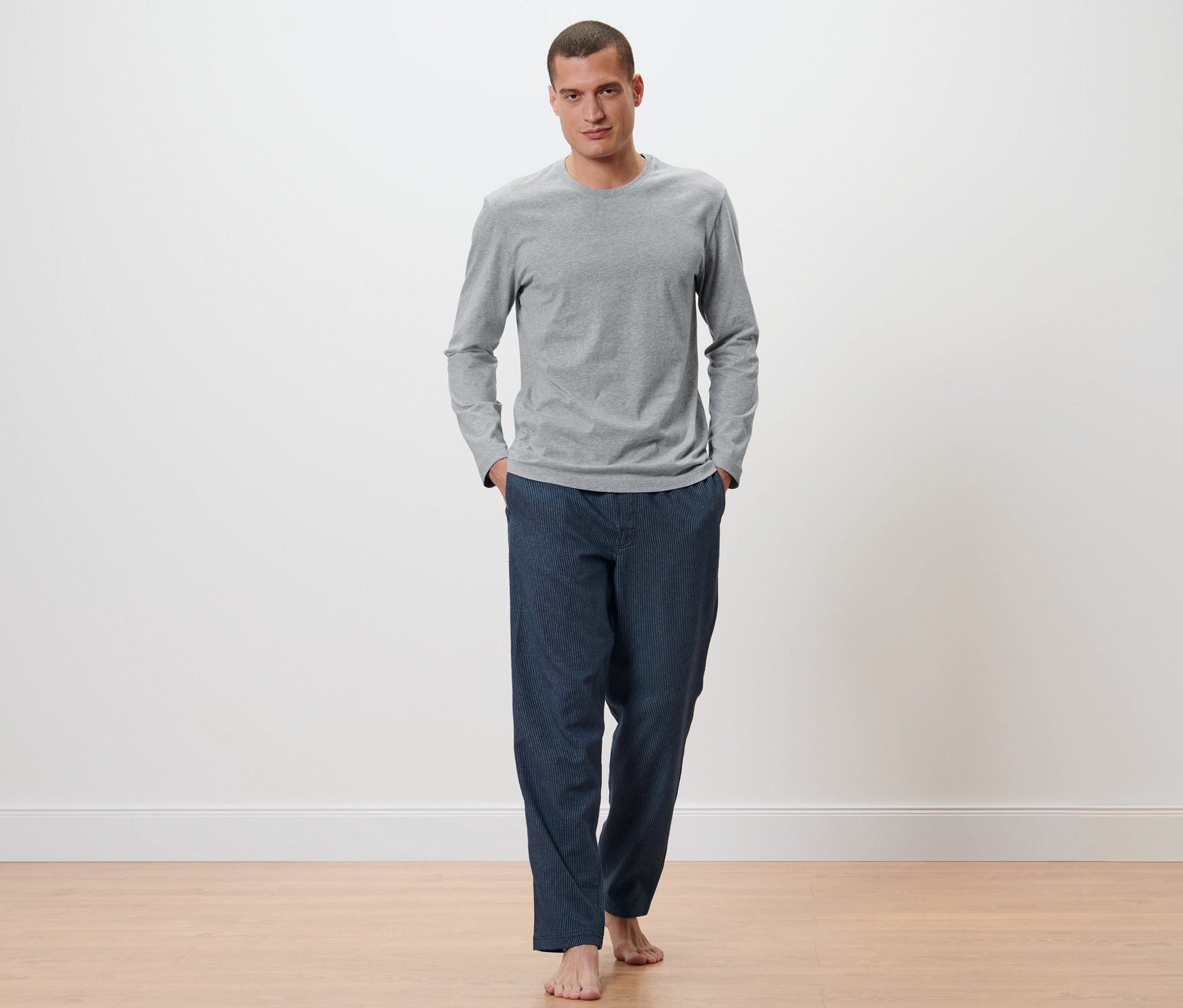 Adam gri renkli, flanel altlı, koyu mavi detaylı erkek pijama takımı giyiyor.