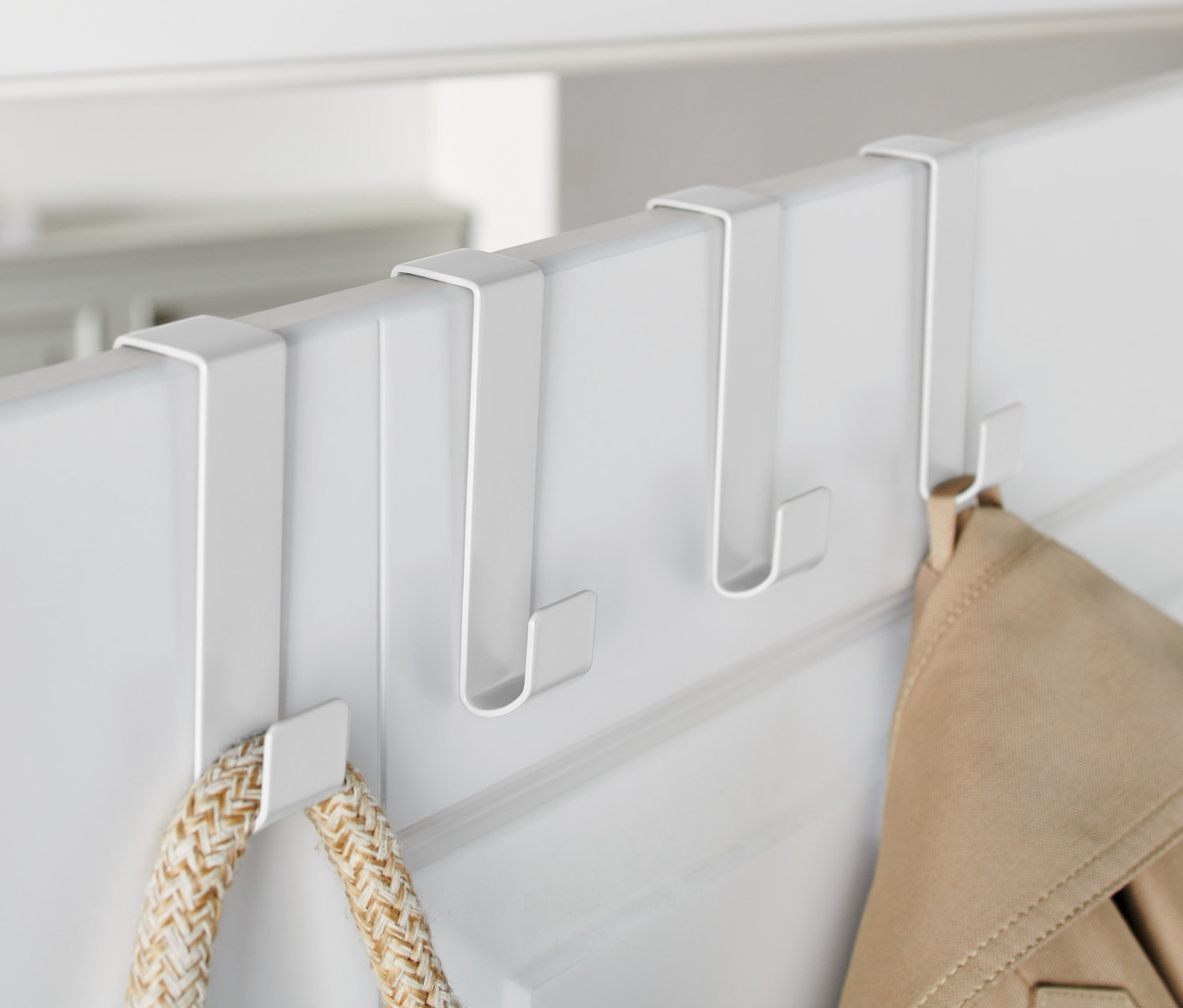 Beyaz bir kapıda asılı duran üç adet beyaz kapı kancası üzerinde bir ceket ve bir çanta asılıdır.