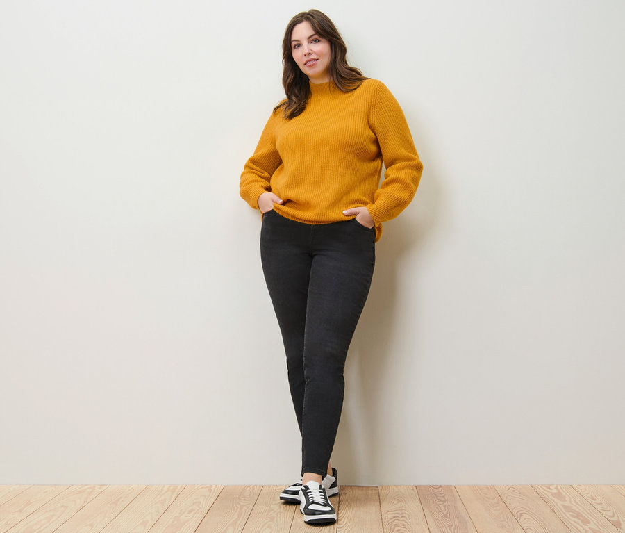 Kadın kalın örgü kazak ve slim fit kot pantolonla poz veriyor.