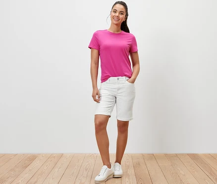 Bir kadın krem beyazı Denim Şort ‒ »Lea« Fit ve pembe bir tişörtle poz veriyor.
