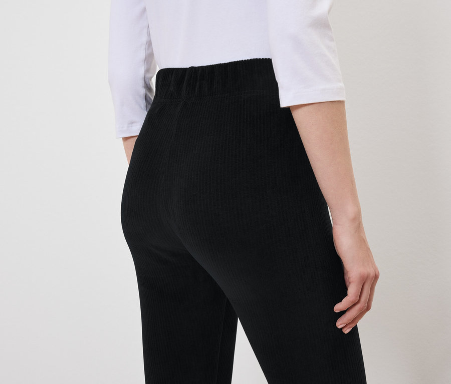 Arkadan görünüşte, siyah kadife pantolon ve beyaz tişört giyen bir kadın var.