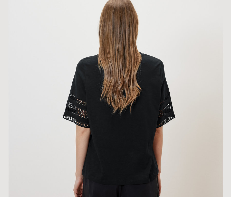 Kahverengi saçlı, siyah nakışlı tişört ve siyah pantolon giyen bir kadının arka görünümü. 