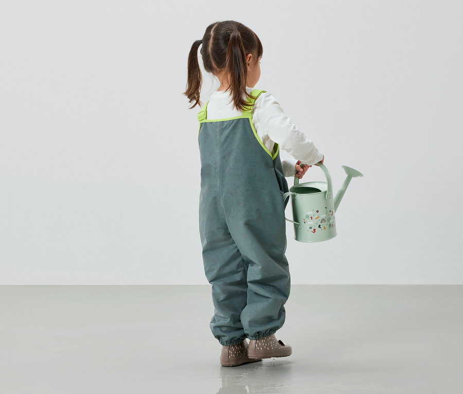Gri pantolonlu kız çocuğu elinde yeşil sulama kabı tutuyor.