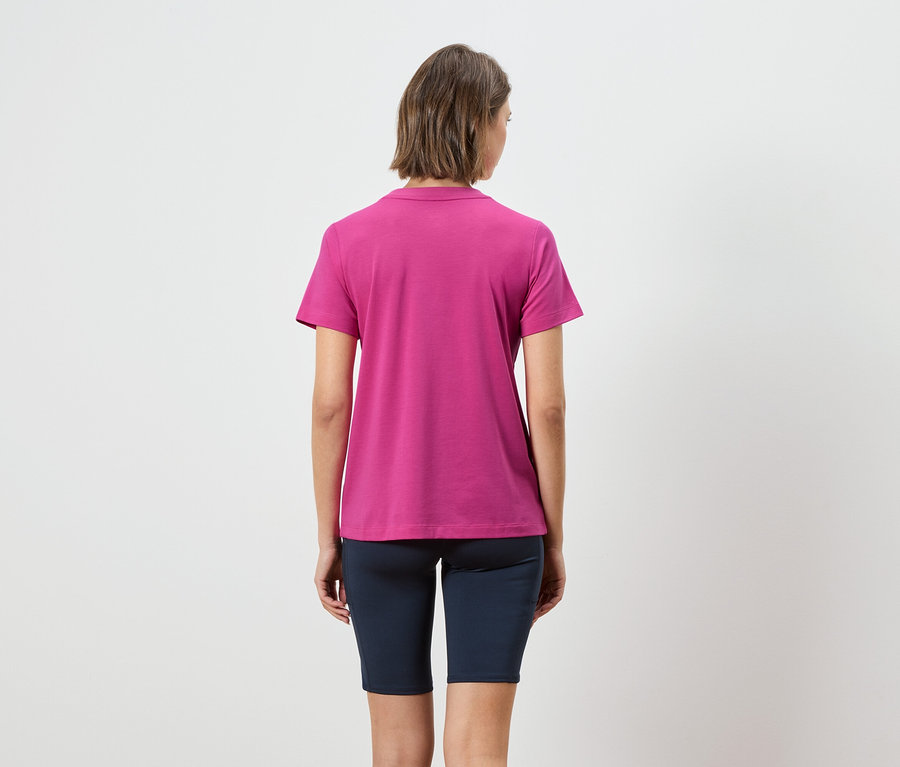 Kısa kahverengi saçlı, pembe polo tişört ve lacivert kısa tayt giyen bir kadının arka görünümü.