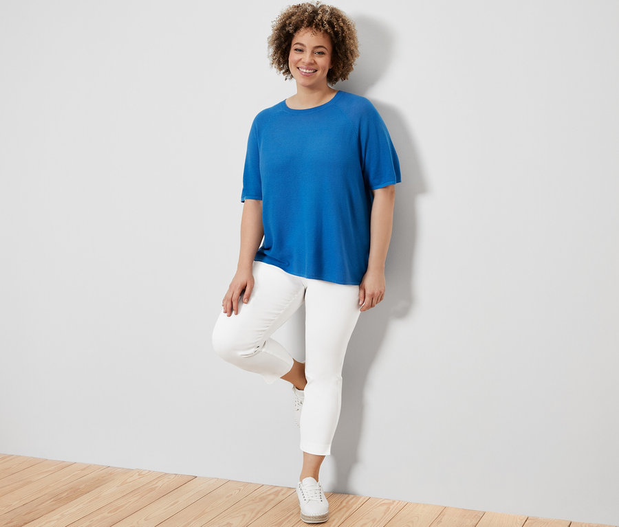 Kadın kobalt mavisi ince triko bluz ve beyaz 7/8 streç pantolonla poz veriyor.