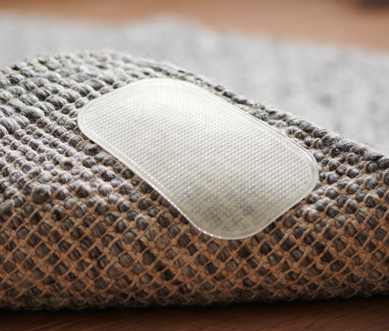 Gri halının köşesinin ve üzerinde şeffaf bir 4 Adet Halı Kaydırmaz'ın yakın çekim görüntüsü.