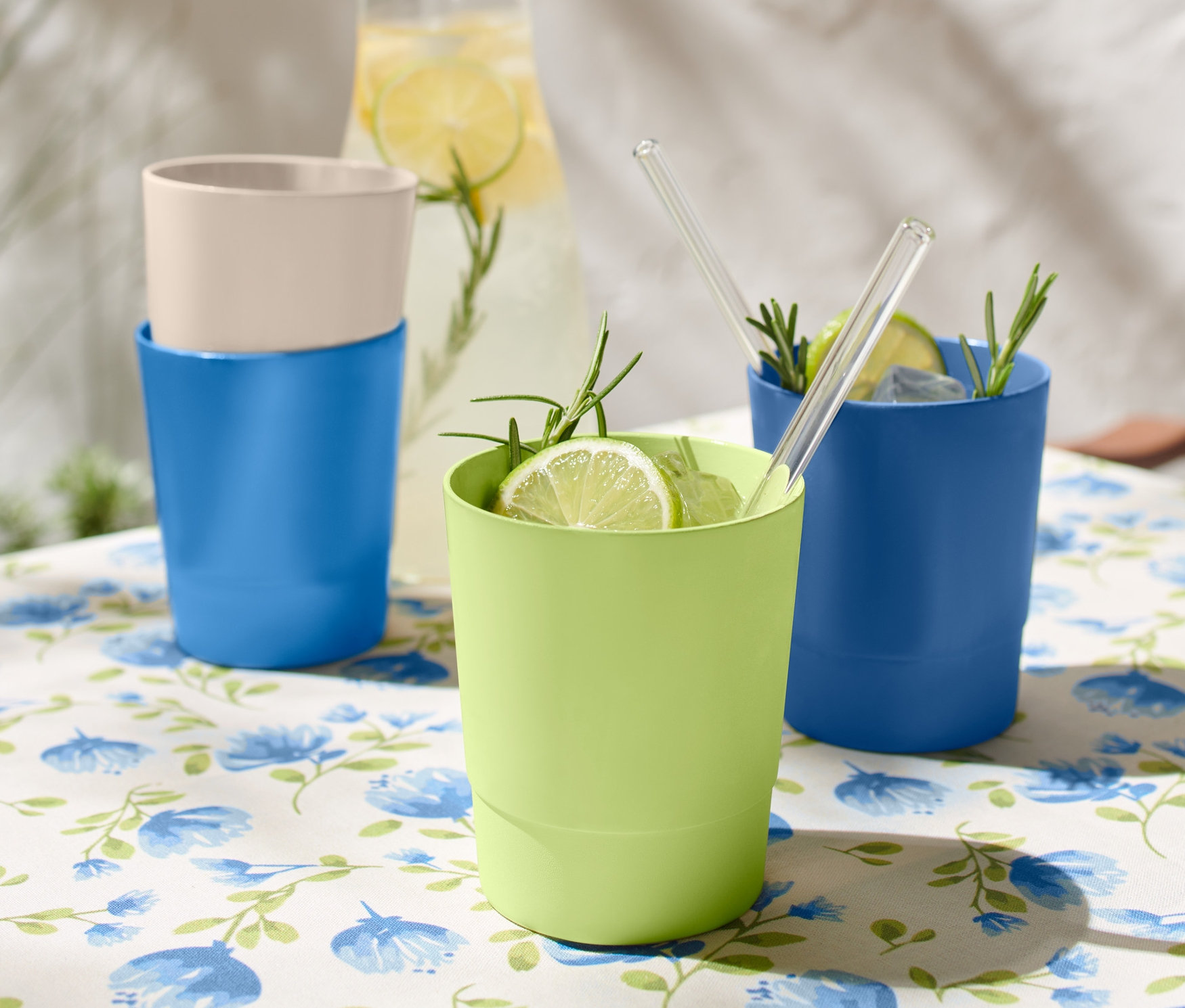 Çiçekli masa örtüsü olan bir masanın üzerinde 4 adet plastik bardak, iki mavi, bir yeşil ve bir bej renkli bardak bulunmaktadır.