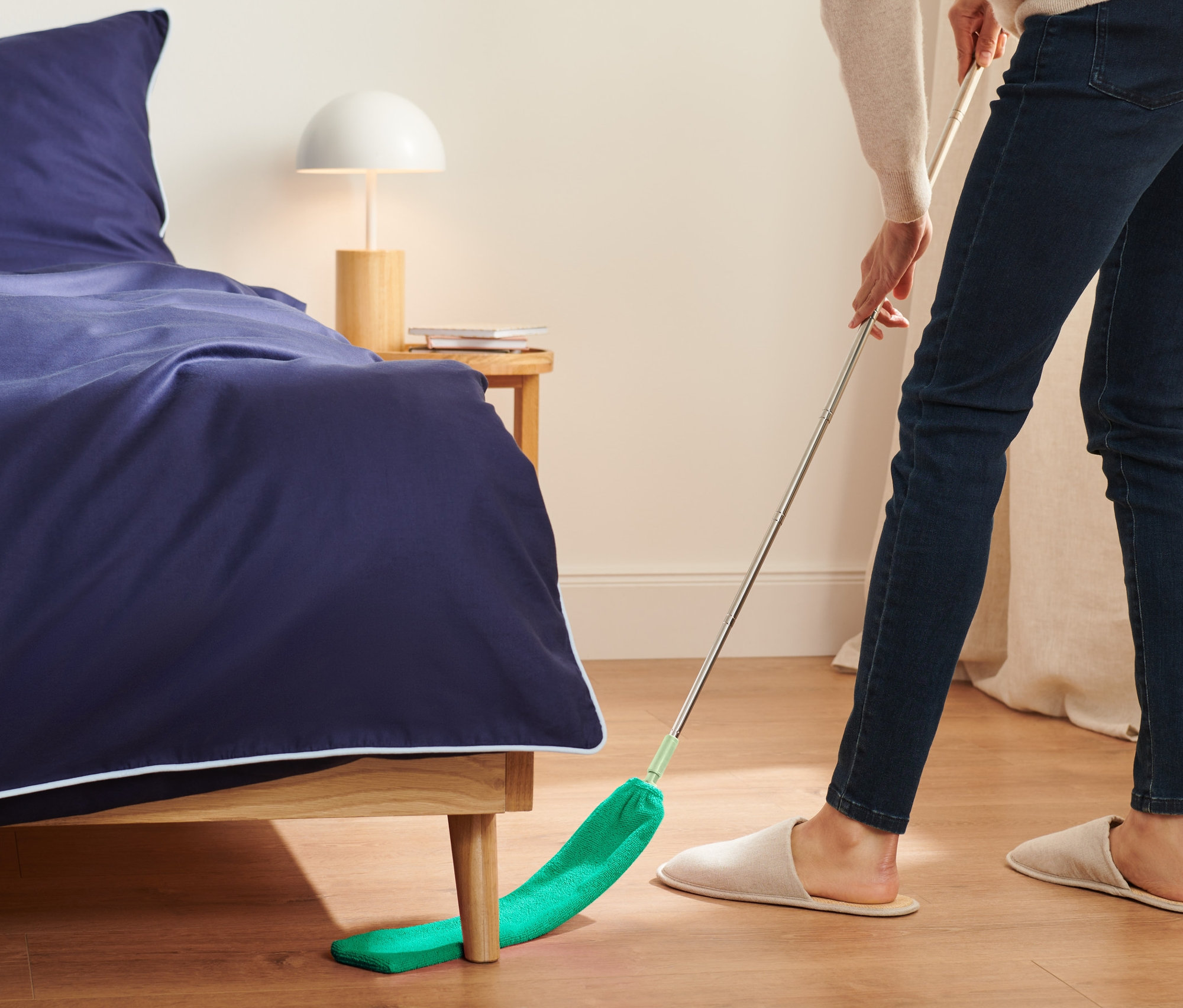 Kadın, yatağın altında Esnek Toz Toplayıcı ile temizlik yapıyor.