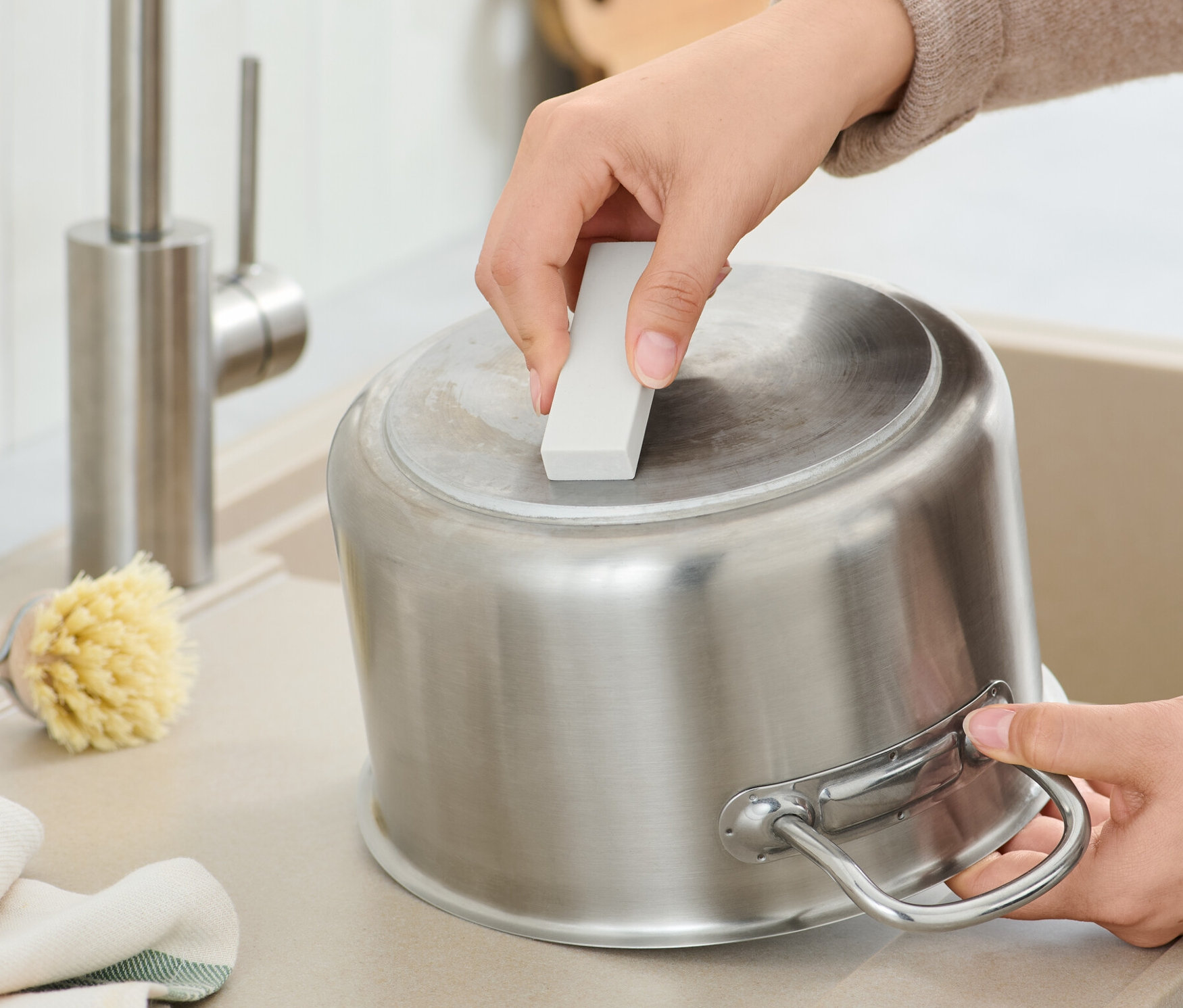 Bir kişi 2 Adet Kireç Silgisi ile paslanmaz çelik bir tencereyi temizliyor.