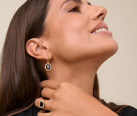 Kadın gülümsüyor ve boynuna dokunuyor, Kraliyet Siyah Kolye, Royal Black Halka Küpe ve Kraliyet Siyahı Yüzük takıyor.