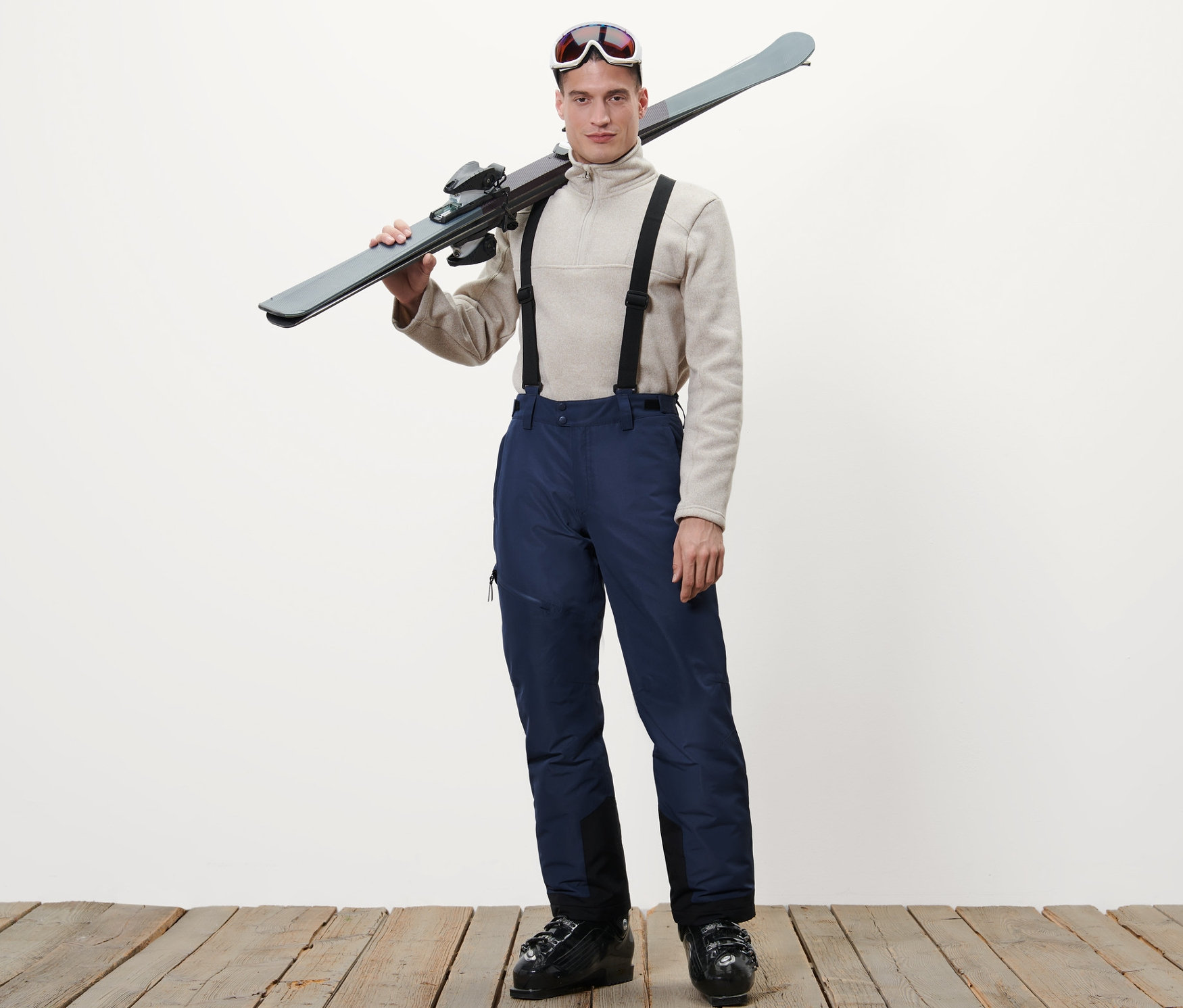 Omzunda kayakları olan adam mavi kayak pantolonu giyiyor.