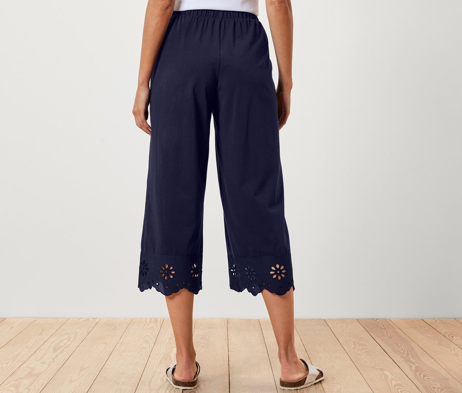 Arkadan görünen, beyaz bir bluz ve etek ucunda nakış detayı bulunan lacivert culotte pantolonlu bir kadın.