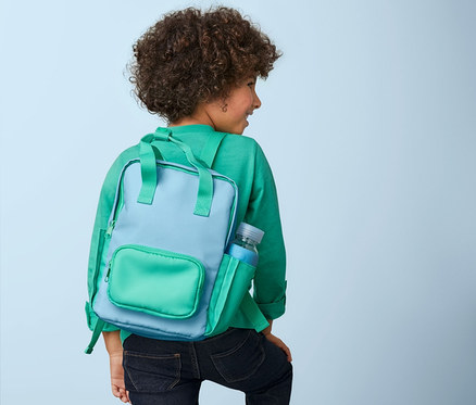 Kıvırcık saçlı bir çocuk merdivenlerden çıkıyor, üzerinde mavi-yeşil Outdoor Sırt Çantası, Mini var.