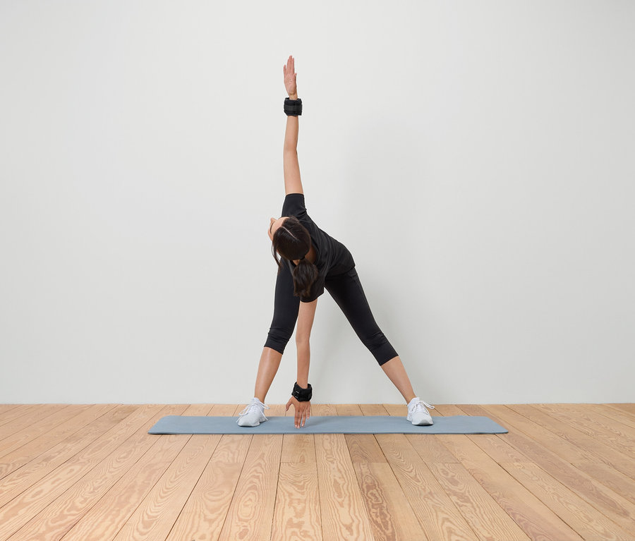 Kadın, bileklerinde ve ayak bileklerinde ağırlıklarla bir mat üzerinde esneme yapıyor.