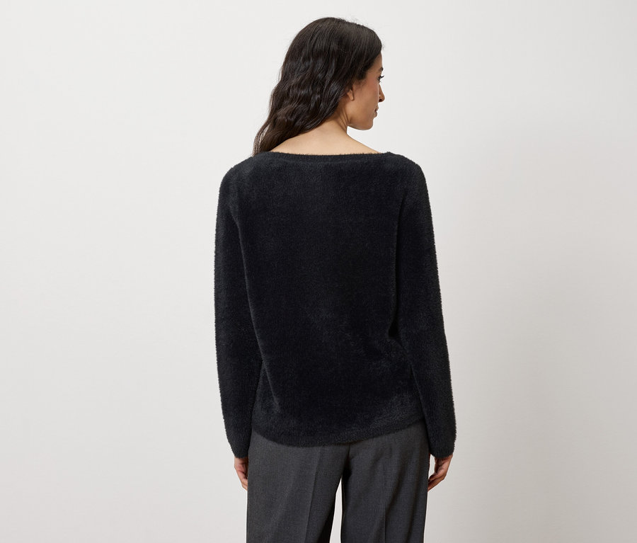 Siyah bir kazak ve gri pantolon giyen bir kadının arka görünümü.