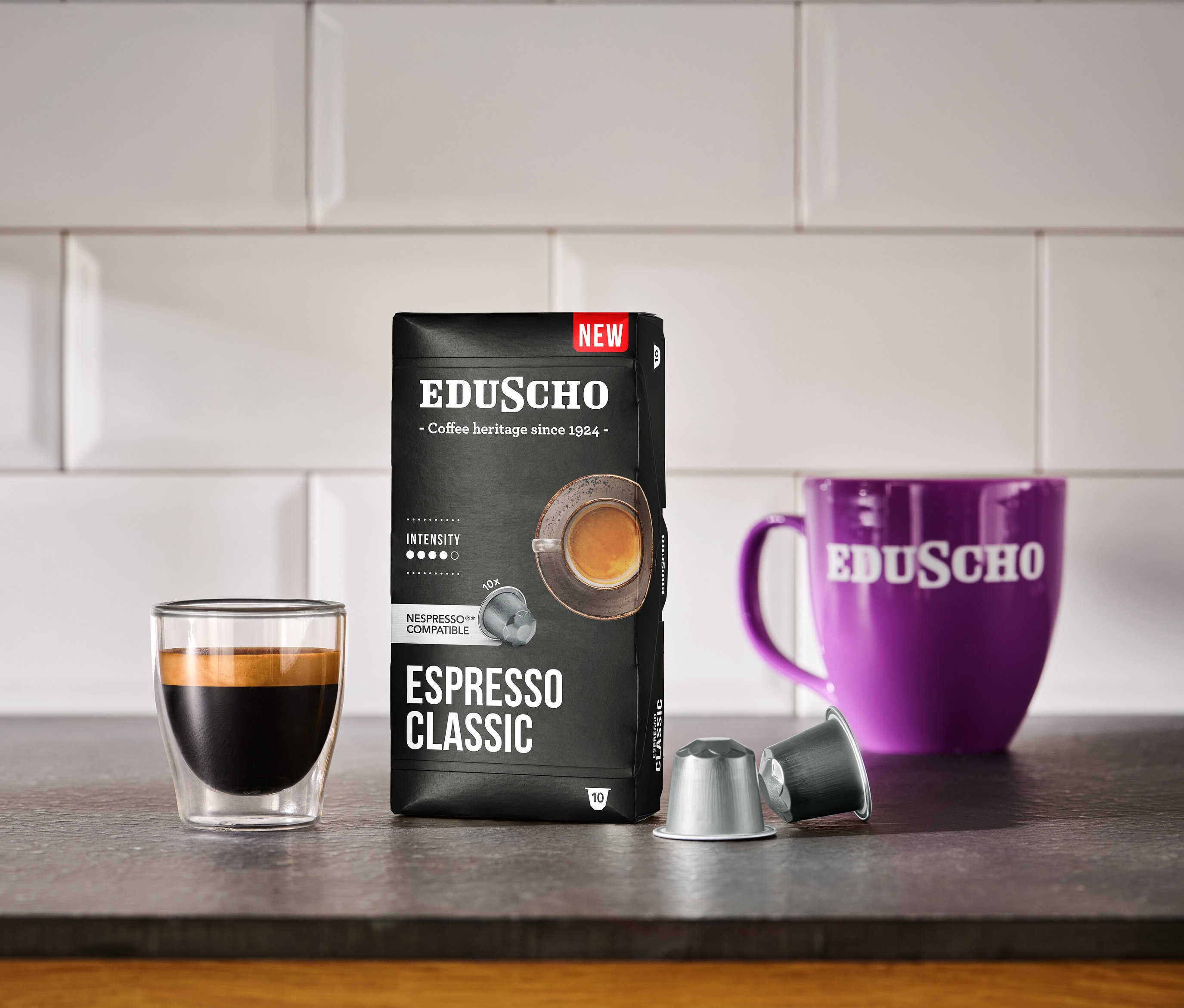 Bir bardak espresso, bir fincan ve iki kahve kapsülü ile birlikte bir paket Eduscho Espresso Classic - 10 kapsülün yanında duruyor.