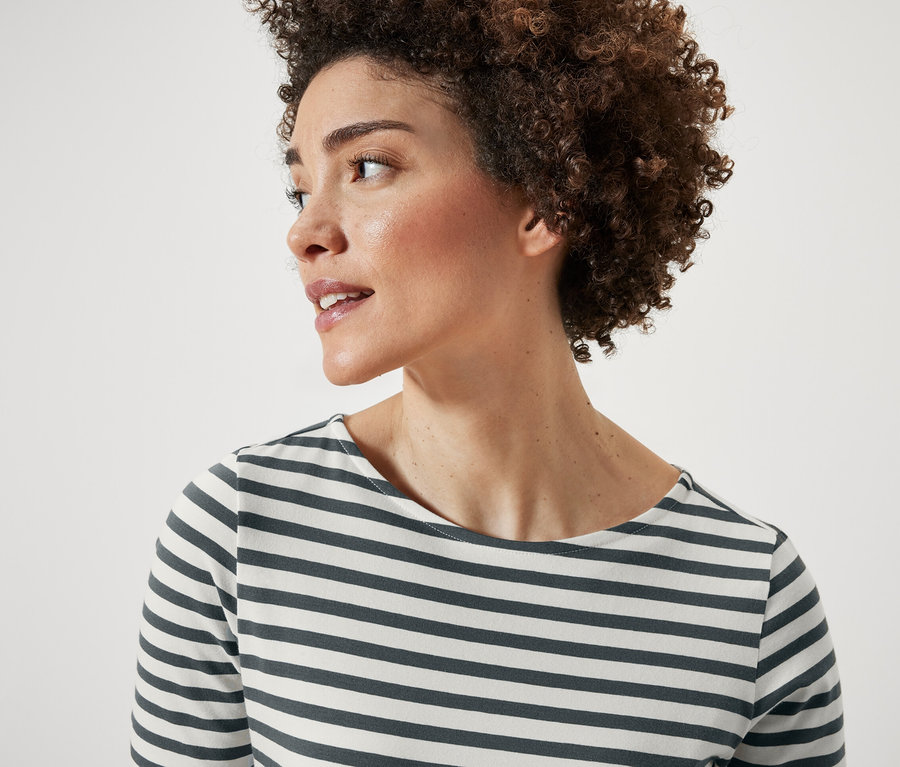 Kısa kıvırcık saçlı bir kadının portresi. Yeşil çizgili, kısa kollu bir tişört giyiyor.