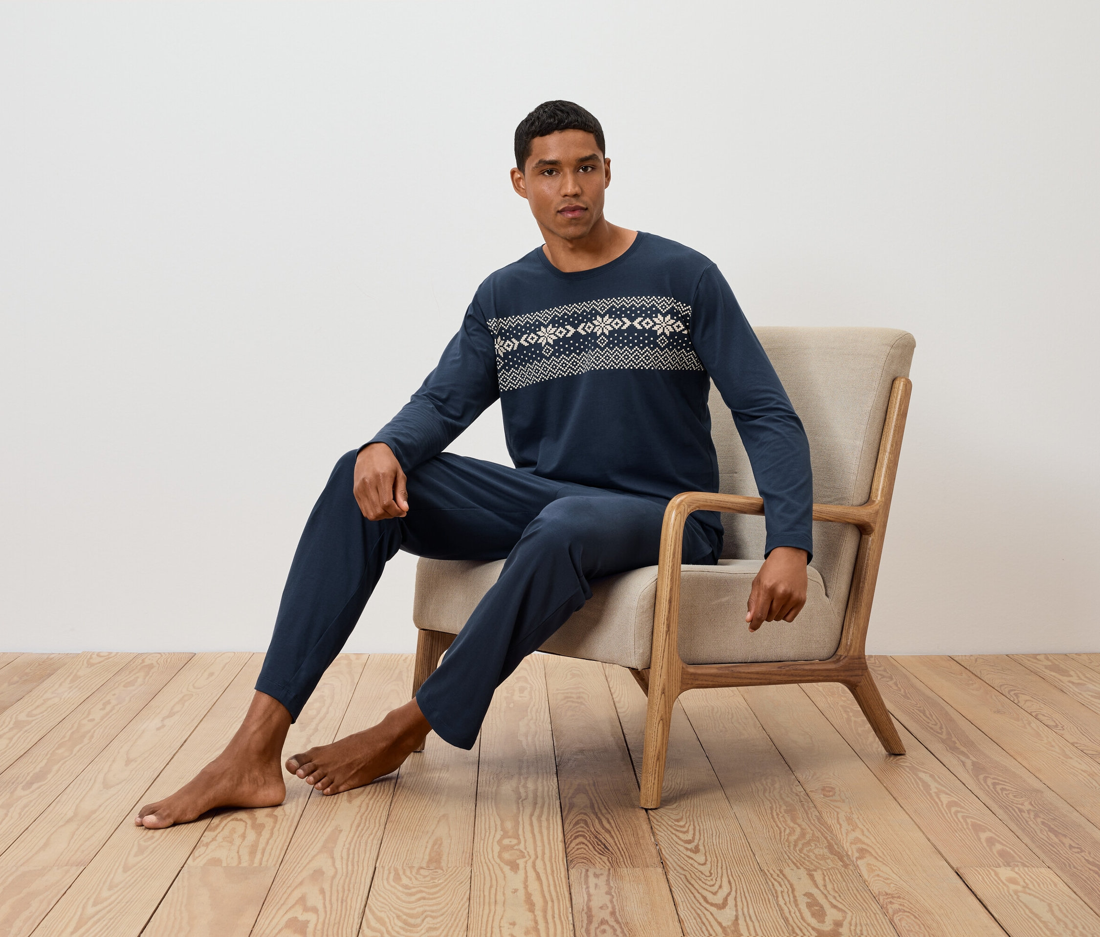 Adam sandalyede oturuyor ve desenli, uzun kollu, lacivert bir pijama giyiyor.