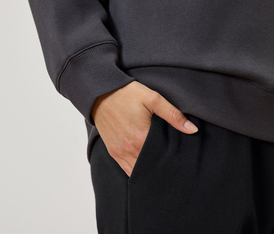 Siyah eşofman altı cebinde eli olan, gri sweatshirt giyen bir kadının yakın çekim detayı.