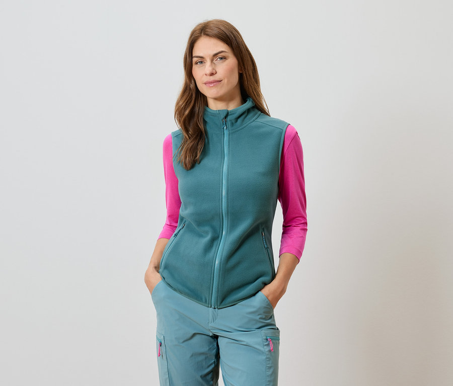 Petrol yelek, uyumlu pantolon ve pembe uzun kollu bluz giyen kadın.