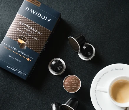 Siyah bir arka planda bir fincan espressonun yanında bir paket ve birkaç kapsül DAVIDOFF CAFÉ Espresso 57 Ristretto.