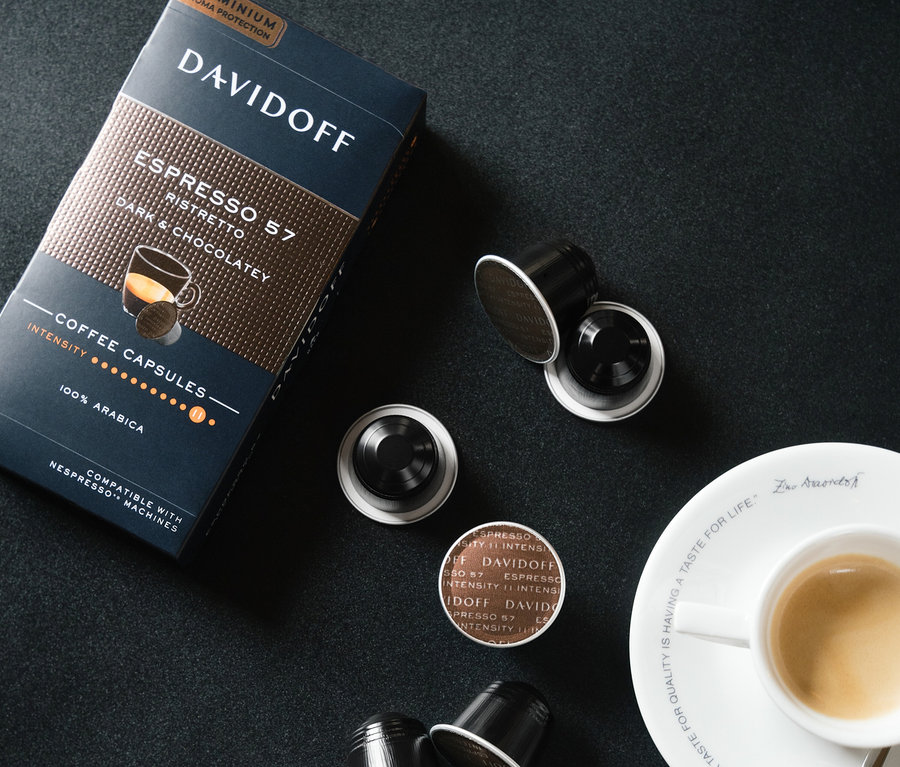 Siyah bir arka planda bir fincan espressonun yanında bir paket ve birkaç kapsül DAVIDOFF CAFÉ Espresso 57 Ristretto.