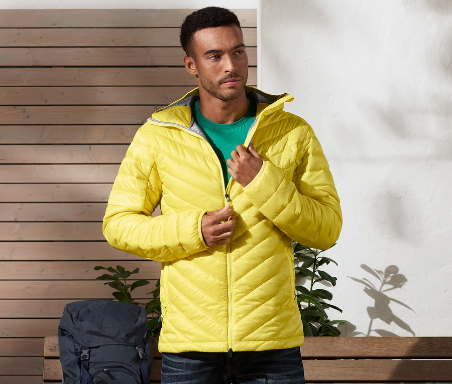 Adam sarı kapitone montunu kapatıyor. Arka planda bir sırt çantası var.