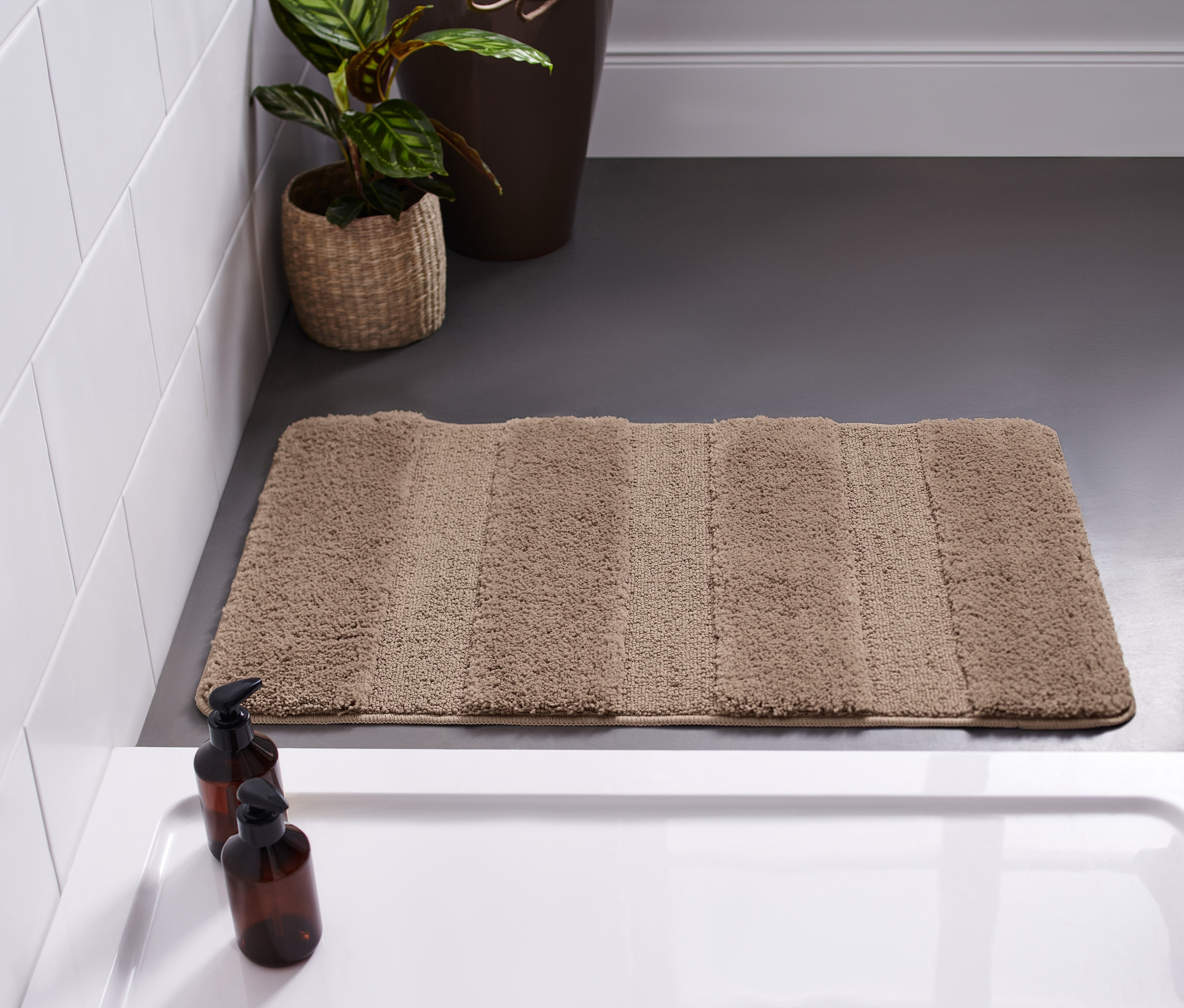 Kahverengi Wellness banyo paspası, yaklaşık 50 x 80 cm, beyaz bir küvetin yanında gri bir zeminde duruyor.