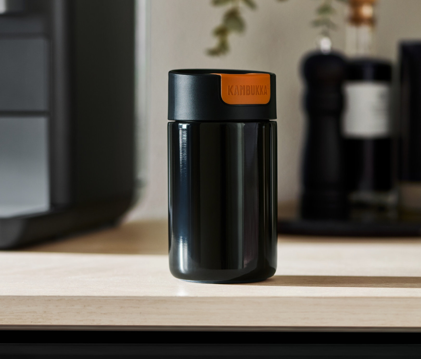 Açık renkli bir masa üzerinde duran siyah bir Kambukka To-Go bardağı.