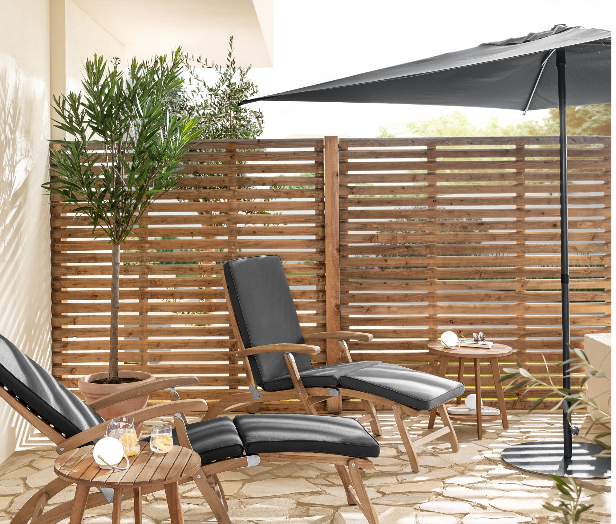 İki adet minderli şezlong ve iki adet 2 Kademeli Yan Sehpa »Lenja« bir terasta duruyor. Bir masanın üzerinde bir Şarjlı Masa Lambası Seti bulunmaktadır.