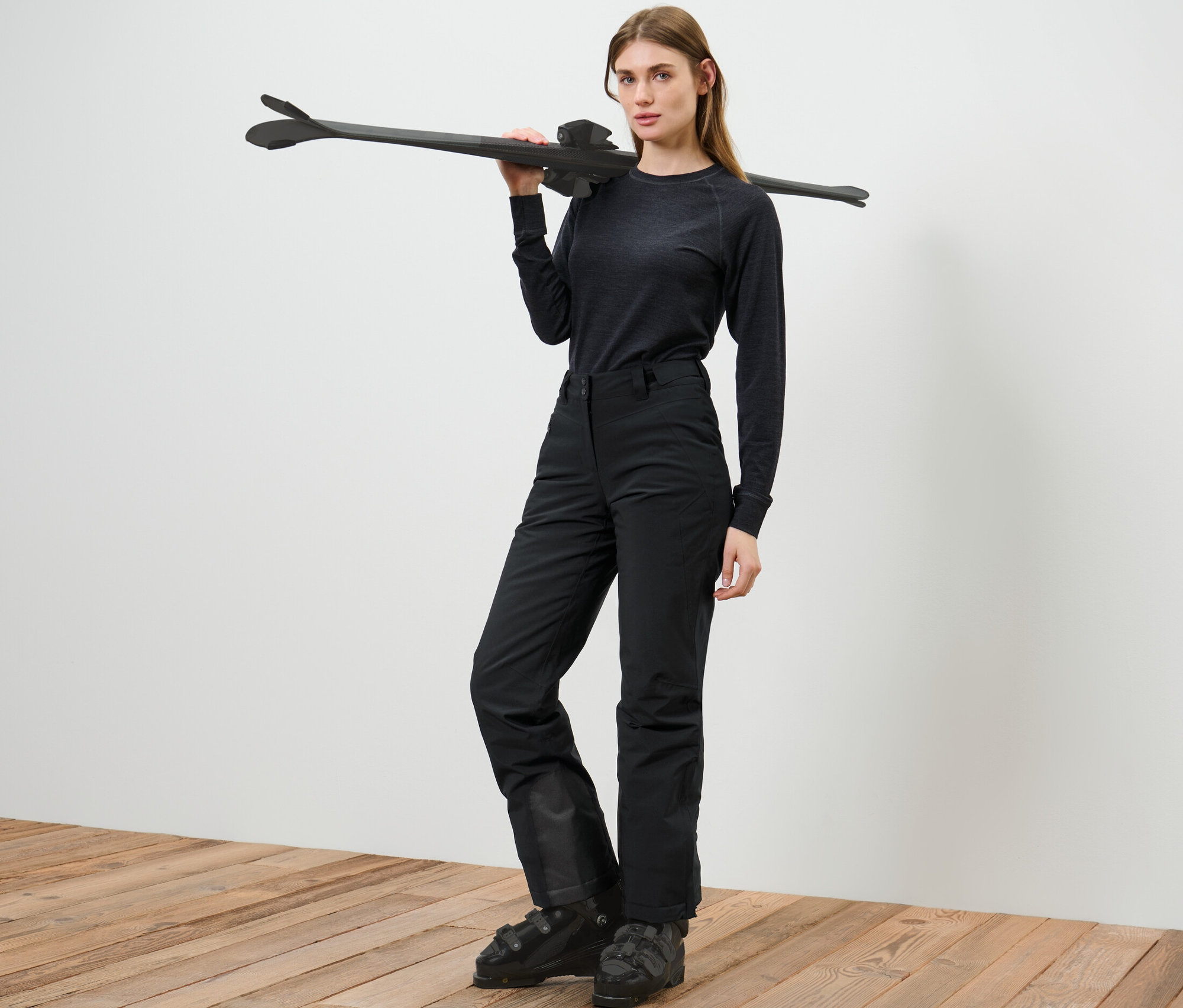 Kadın kayak pantolonuyla poz veriyor ve omzunda kayak taşıyor.