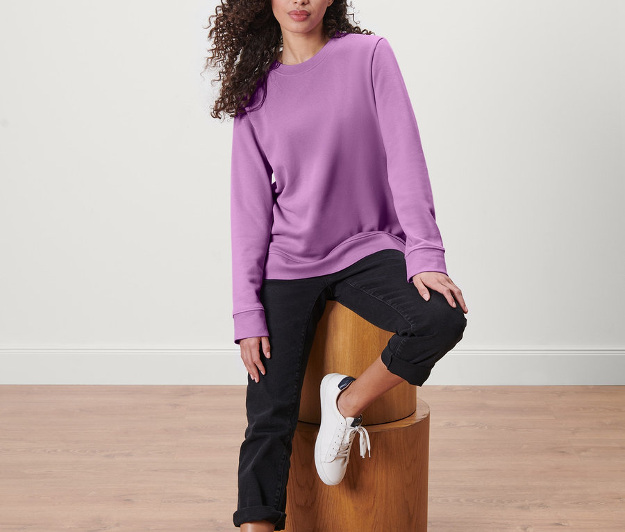 Kadın ahşap bir taburede oturuyor ve sweatshirt giyiyor.