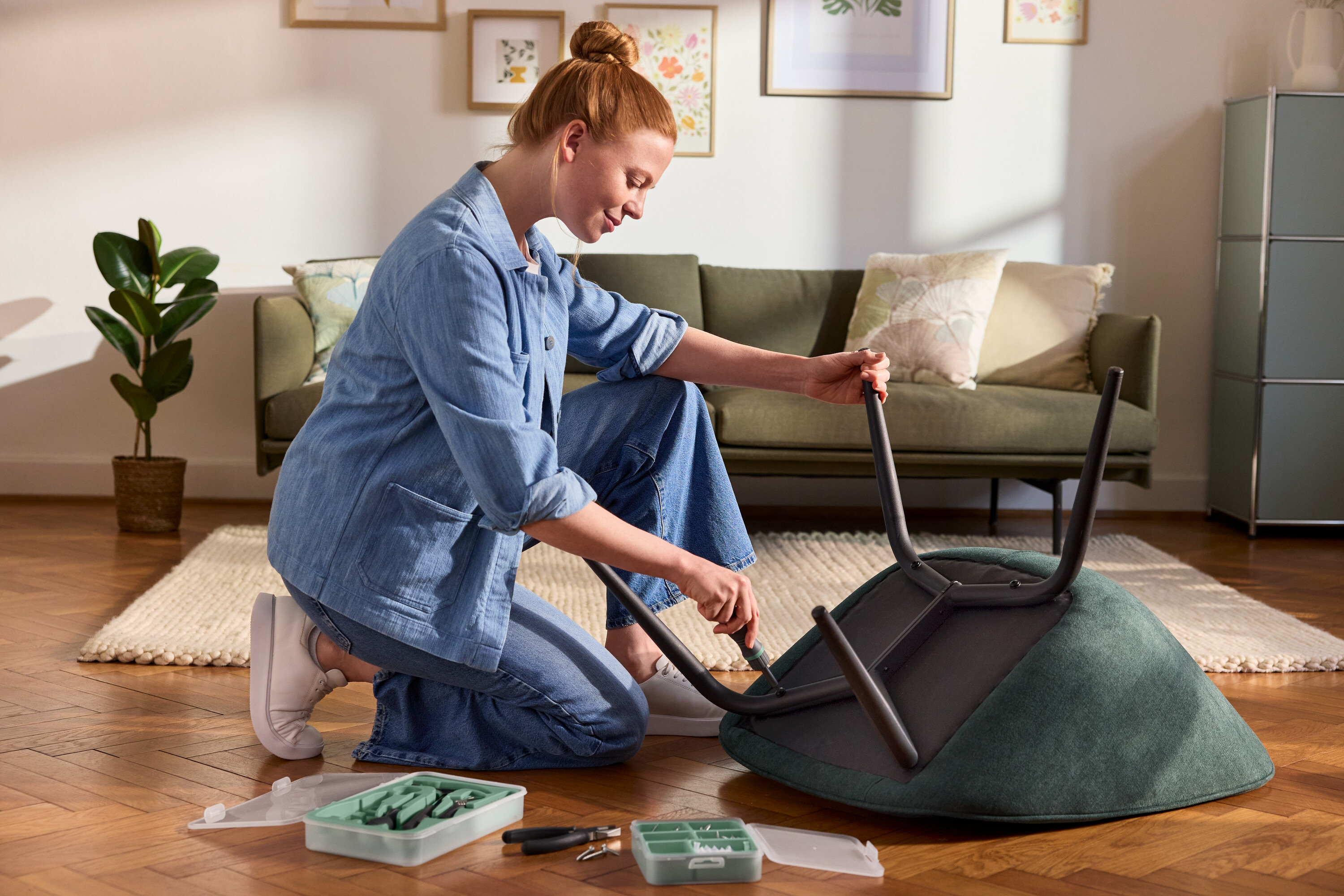 Bir kadın diz çökmüş halde bir alet setinden manyetik bir tornavida ile bir sandalyenin ayaklarını takıyor. Yakınlarda bir vida ve dübel seti var.